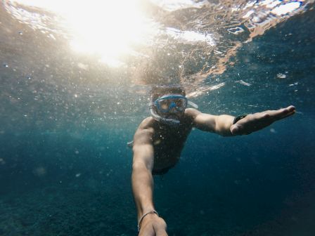A person underwater is snorkeling with a mask and snorkel, reaching out with one arm, and the sunlight is filtering through the water's surface.