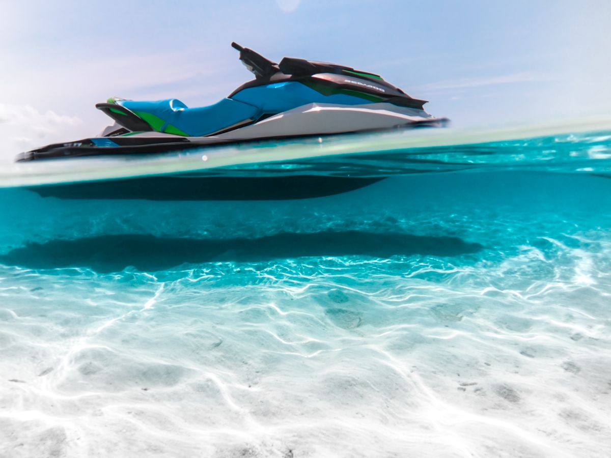 A jet ski floats on crystal-clear turquoise water with a white sandy bottom visible beneath the surface, and a horizon of blue sky.