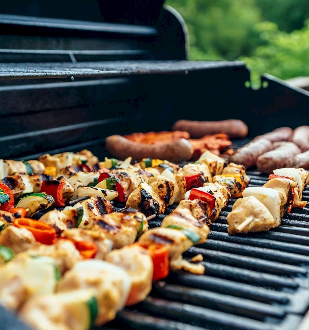 Grilled chicken and vegetable kebabs with sausages sizzle on a backyard barbecue grill.