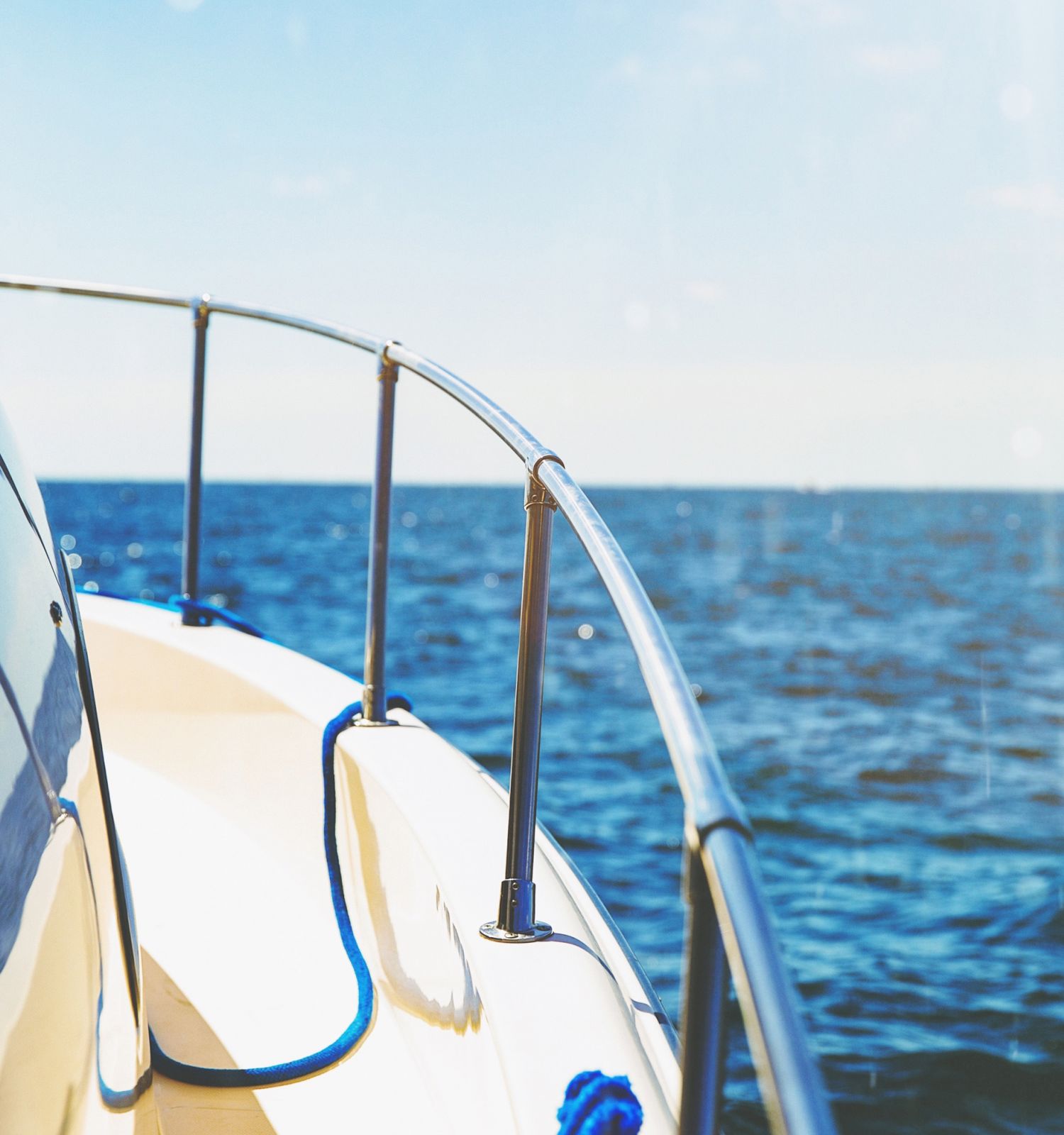 The image shows the side of a boat with a railing, blue rope, and the ocean in the background on a sunny day.