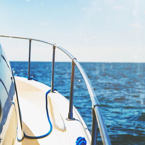 A close-up view of a boat's deck and railing, with a blue rope visible, sailing on a calm sea under a clear blue sky.