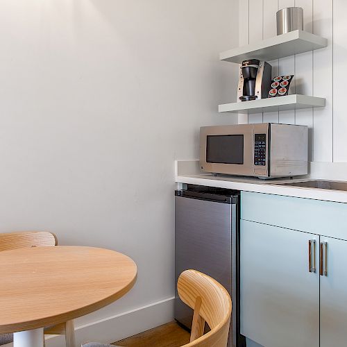 A small kitchenette featuring a sink, microwave, refrigerator, coffee maker, and a round wooden table with two chairs.