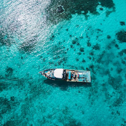 Aerial view of a boat floating on clear blue waters with visible underwater reefs and patches, creating a serene and picturesque scene.