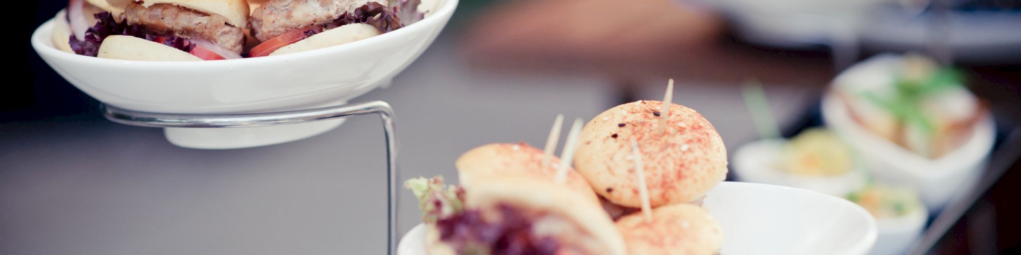 The image shows small gourmet sliders arranged on white dishes, displayed on a tiered metal stand.