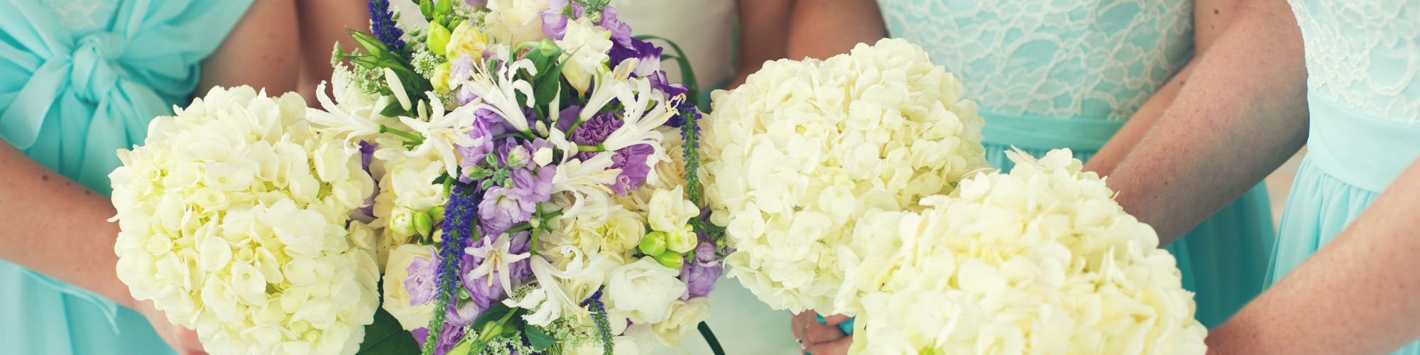 A bride and three bridesmaids in light blue dresses hold bouquets of white and purple flowers. The image highlights their floral arrangements.