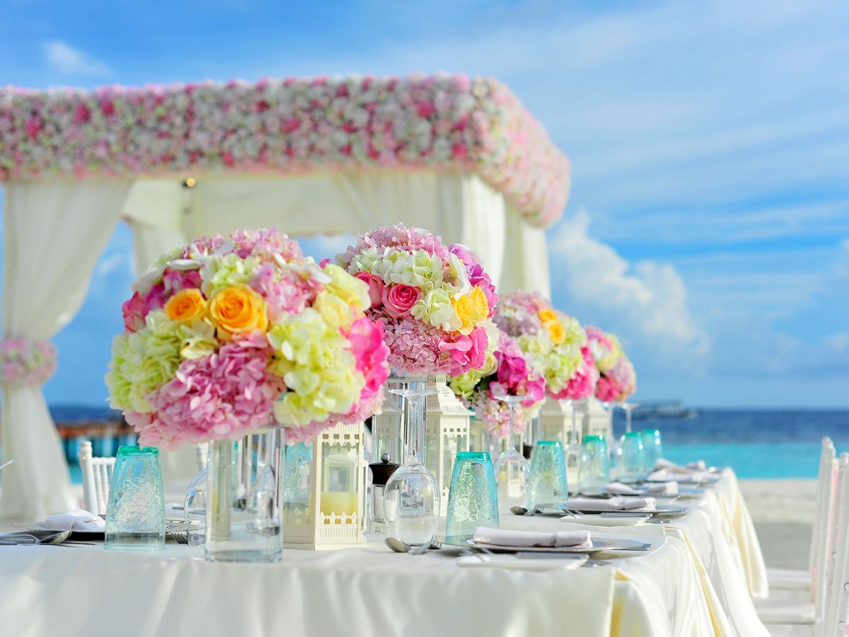 A beautifully set table at an outdoor event with colorful flower arrangements under a canopy, overlooking the ocean on a bright, sunny day.