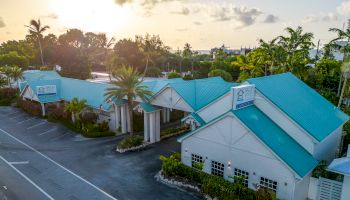 The image shows a building complex with teal roofs and palm trees, likely a commercial or public facility, situated along a road during sunset.