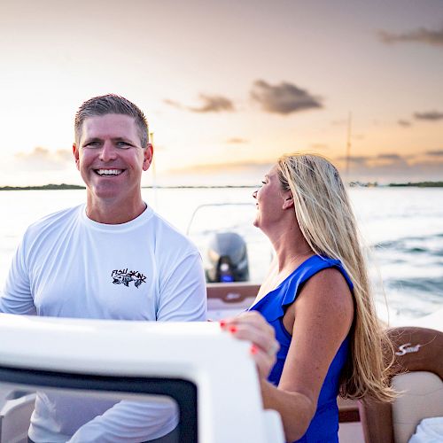 A man and a woman are on a boat at sunset, smiling and enjoying the time on the water, with the horizon in the background.