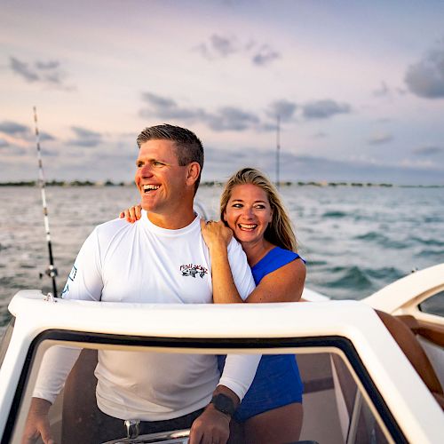 A man and woman enjoying a boat ride at sunset, with fishing rods in the background and a water bottle on the boat's console.