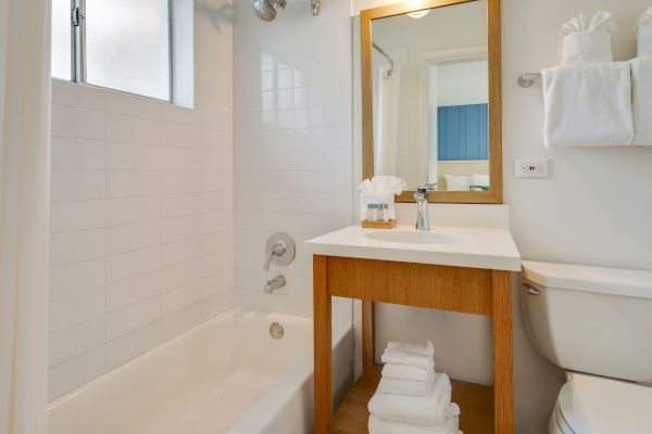 A clean, modern bathroom featuring a bathtub, a wooden vanity with a sink and mirror, a toilet, and neatly arranged towels in a compact space.