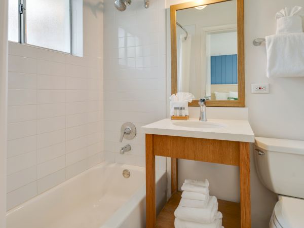 A clean, modern bathroom featuring a bathtub, a wooden vanity with a sink and mirror, a toilet, and neatly arranged towels in a compact space.