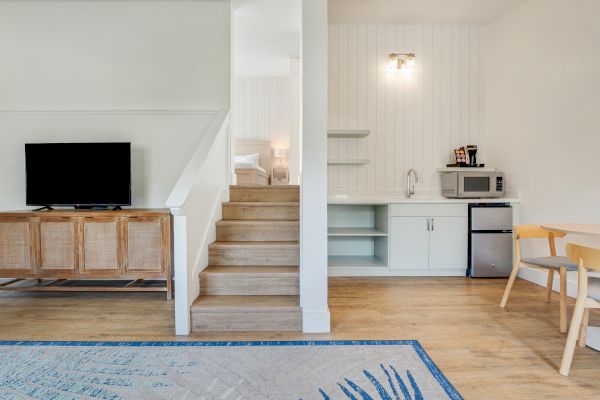 A modern interior featuring a split-level room with a TV, kitchenette, dining area, stairs leading to a bed, and a cozy carpet on wooden flooring.