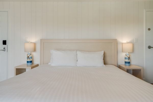 A neatly made bed with white linens, flanked by nightstands with identical lamps and light-colored walls, creates a serene ambiance.