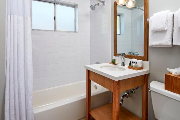 A clean, modern bathroom featuring a bathtub with a shower, a vanity with a mirror and sink, towels, and a toilet with a tissue box.