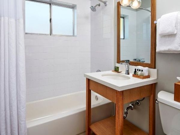 A bright bathroom with a white sink vanity, wooden mirror frame, toiletries, towels, and a shower curtain.