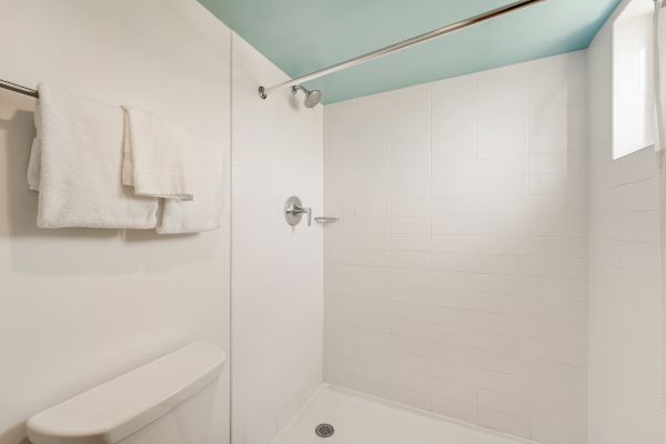This image shows a clean, white bathroom with a shower area, a towel hanging on a rod, and a portion of a toilet visible on the left.