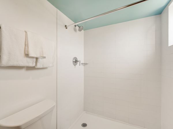 This image shows a clean, white bathroom with a shower area, a towel hanging on a rod, and a portion of a toilet visible on the left.