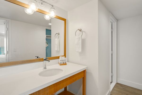 A modern bathroom vanity with a large mirror, a sink, and a wooden frame. The white wall has a towel ring with a folded towel hanging.