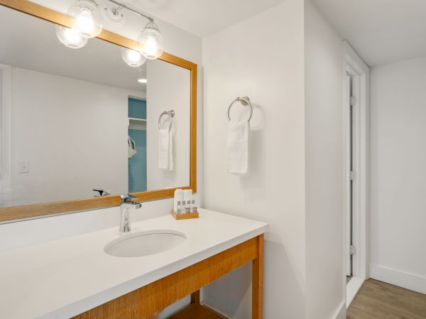 A modern bathroom vanity with a large mirror, a sink, and a wooden frame. The white wall has a towel ring with a folded towel hanging.