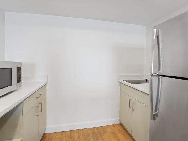 A small kitchen with light-colored cabinets, a microwave on the counter, a stainless steel refrigerator, and a stainless steel sink.