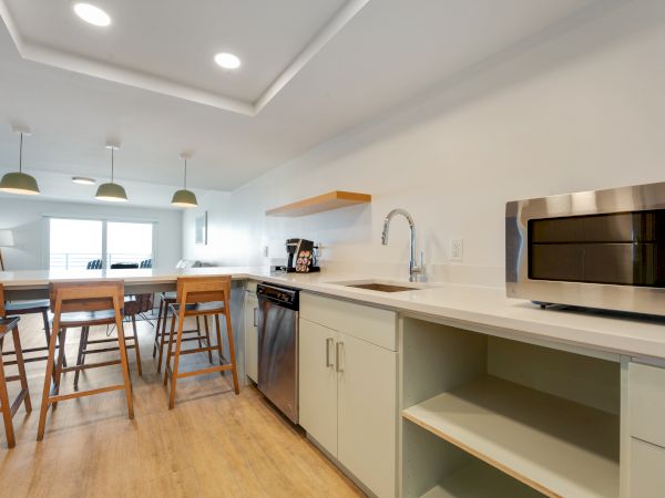 This image shows a modern kitchen with wooden stools at a counter, a sink, a dishwasher, and a microwave on a white countertop, ending the sentence.