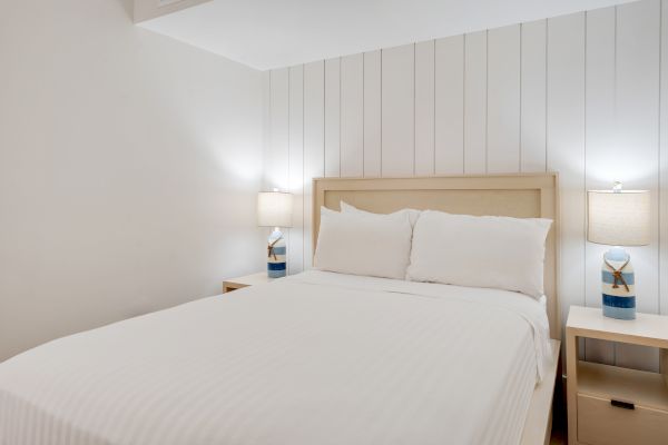 The image shows a minimalist bedroom with a bed centered between two nightstands, each with a lit table lamp.