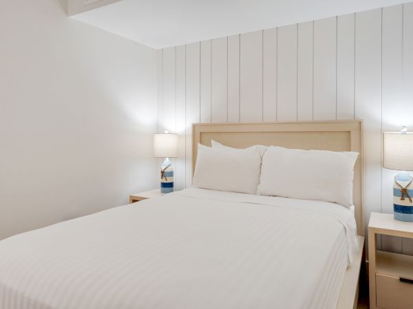The image shows a minimalist bedroom with a bed centered between two nightstands, each with a lit table lamp.