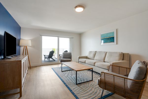 A modern living room features a couch, armchair, coffee table, TV stand, and lamp, with a patio door leading to a balcony. The sentence ends.