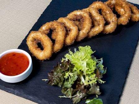 Crispy onion rings, a side salad, and a cup of red dipping sauce on a slate plate.