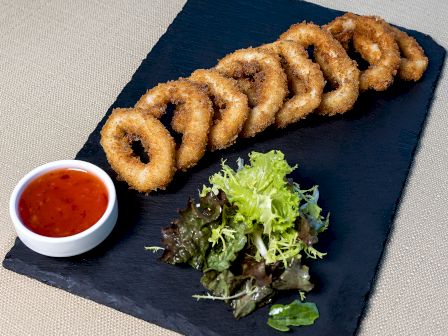 This image shows a platter with crispy fried calamari rings, a side of mixed greens, and a small bowl of dipping sauce.