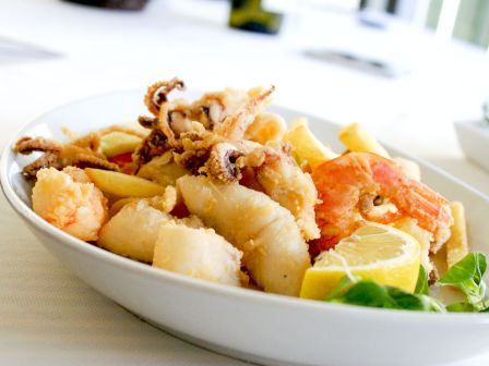 A plate of mixed fried seafood and fries with lemon wedges and leafy greens.