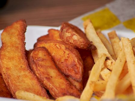 A plate of crispy fried potato wedges and fries, golden and seasoned for snacking.