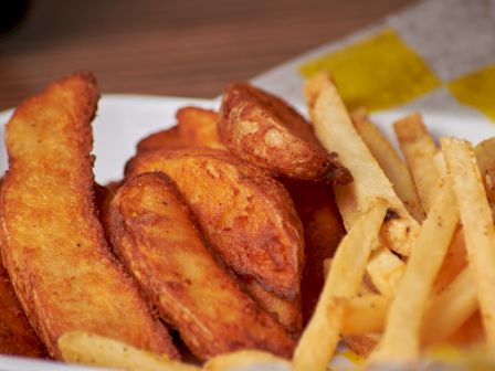 The image shows a white plate filled with crispy potato wedges and french fries, with a napkin in the background.