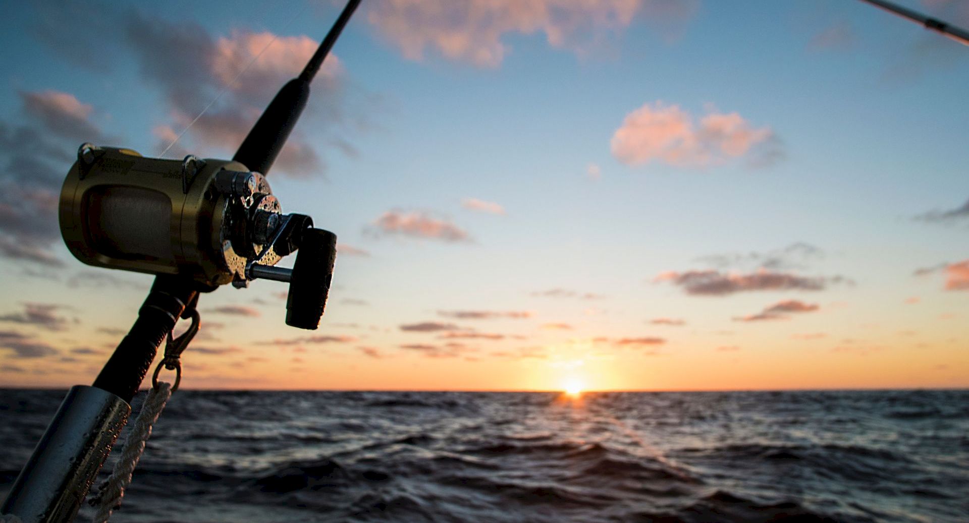 A ship&rsquo;s cannon points over the ocean at sunset, with waves rolling beneath a colorful sky.