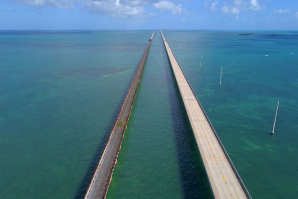 The image shows two long parallel bridges stretching over a large body of water with clear skies and some clouds in the background.