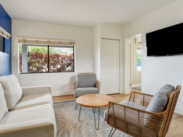 A modern living room with a sofa, two chairs, a round coffee table, wall-mounted TV, large window, and blue accent wall.