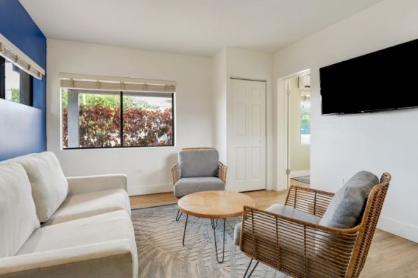 A modern living room with a sofa, two chairs, a round coffee table, wall-mounted TV, large window, and blue accent wall.