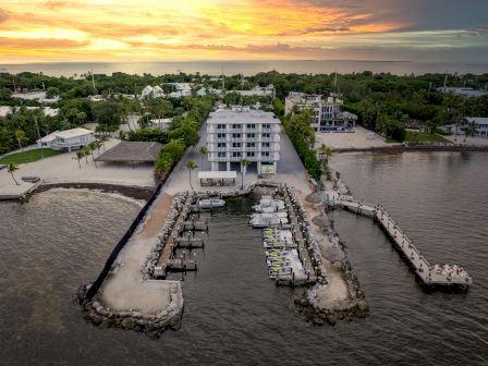 A sunset view of a waterfront property with a central building, surrounding homes, docks with boats, and piers extending into the water.