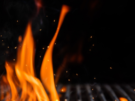 This image shows flames rising from a grill with sparks visible, set against a dark background.