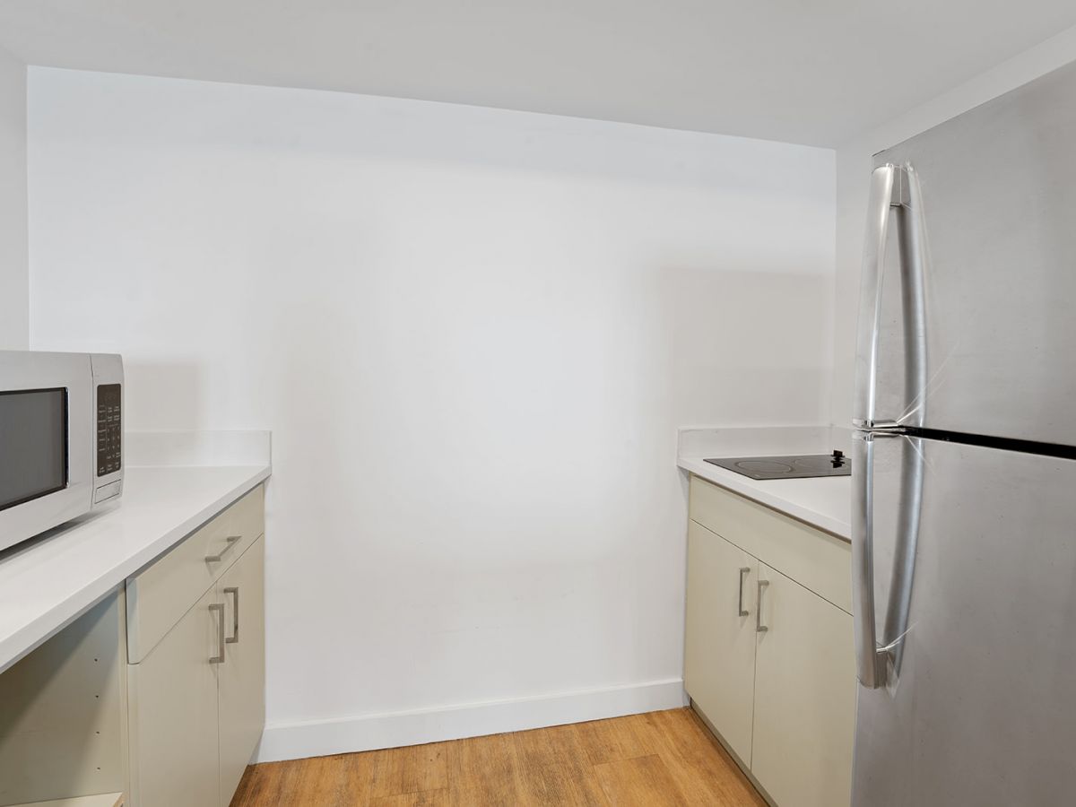 A small kitchen with white walls, a microwave on the counter, cabinets below, a stainless steel refrigerator, and a sink on the right.