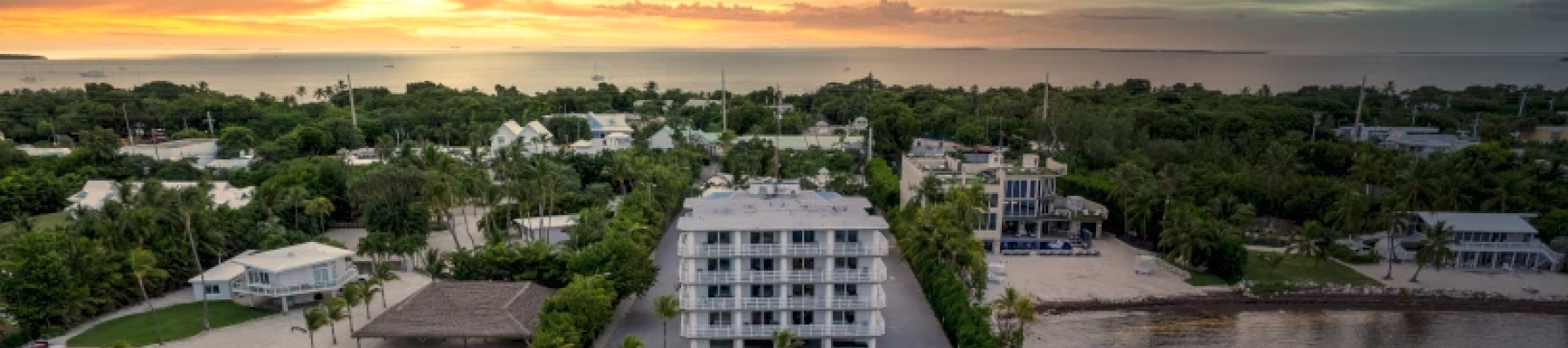 An aerial view of a waterfront hotel with docks, surrounded by trees and a sunset sky.