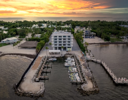 An aerial view of a waterfront hotel with docks, surrounded by trees and a sunset sky.