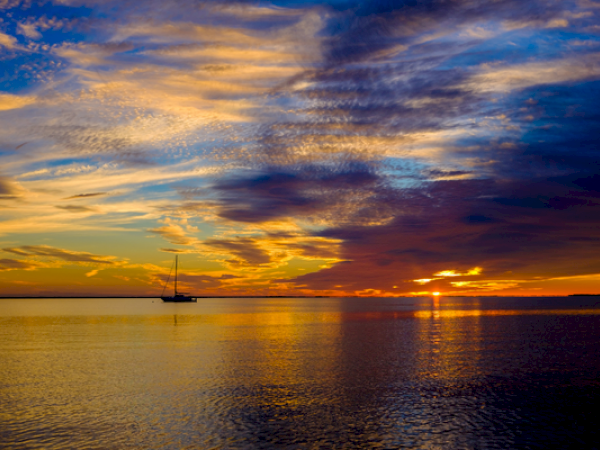 A serene seascape at sunset, vibrant skies with a boat silhouetted on the calm water.