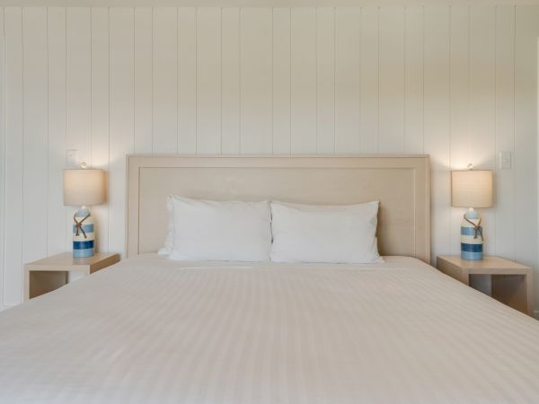 A neatly made bed with white linens, flanked by nightstands with identical lamps and light-colored walls, creates a serene ambiance.