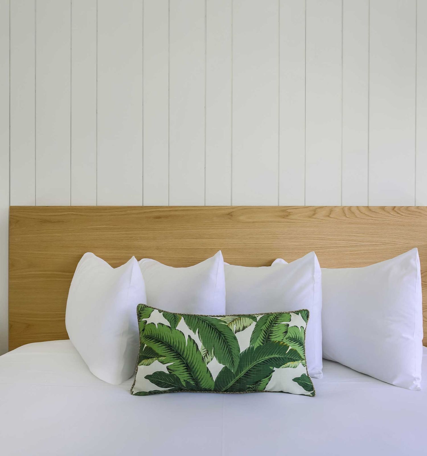 A neatly made bed with white pillows and a green leaf-patterned pillow, flanked by two nightstands with matching lamps and a wooden headboard.