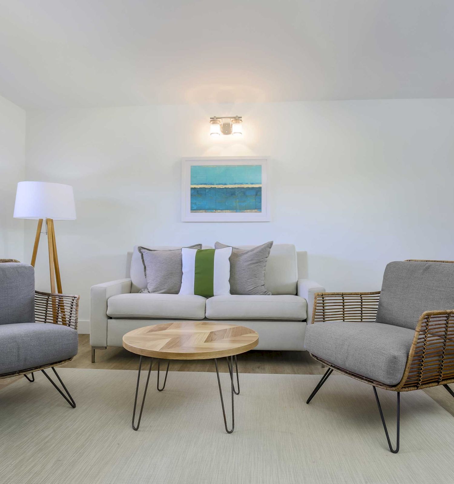 A modern living room with two armchairs, a white sofa, a round wooden coffee table, a floor lamp, a wall painting, and a TV on a wooden cabinet.