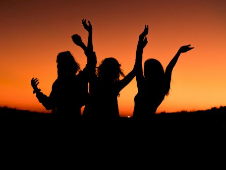 Three people with raised arms silhouetted against an orange sunset sky.